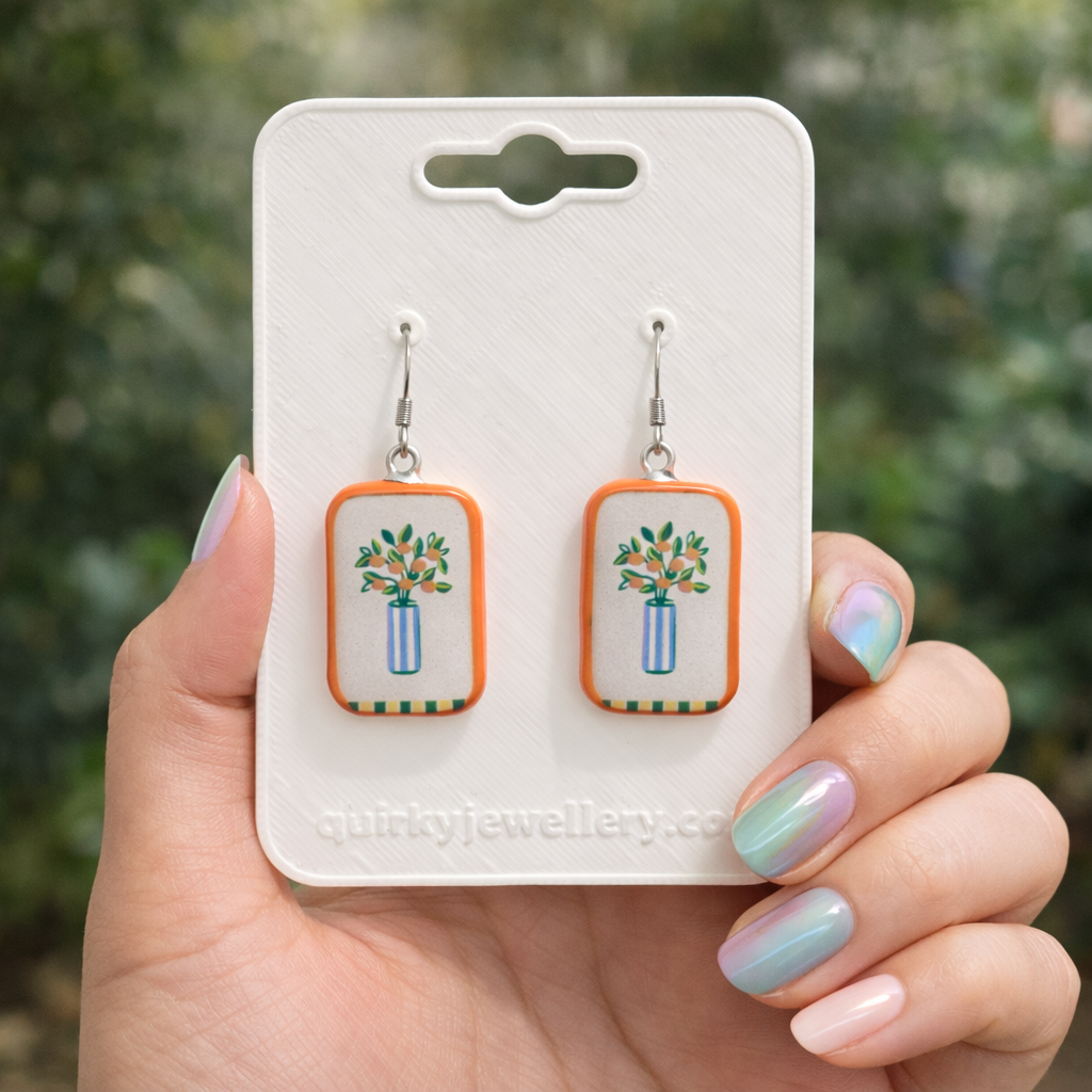 Earrings on a 'quirkyjewellery.com' card held by a hand with pastel nail polish.