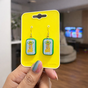 Earrings on a yellow card held by a hand in an indoor setting