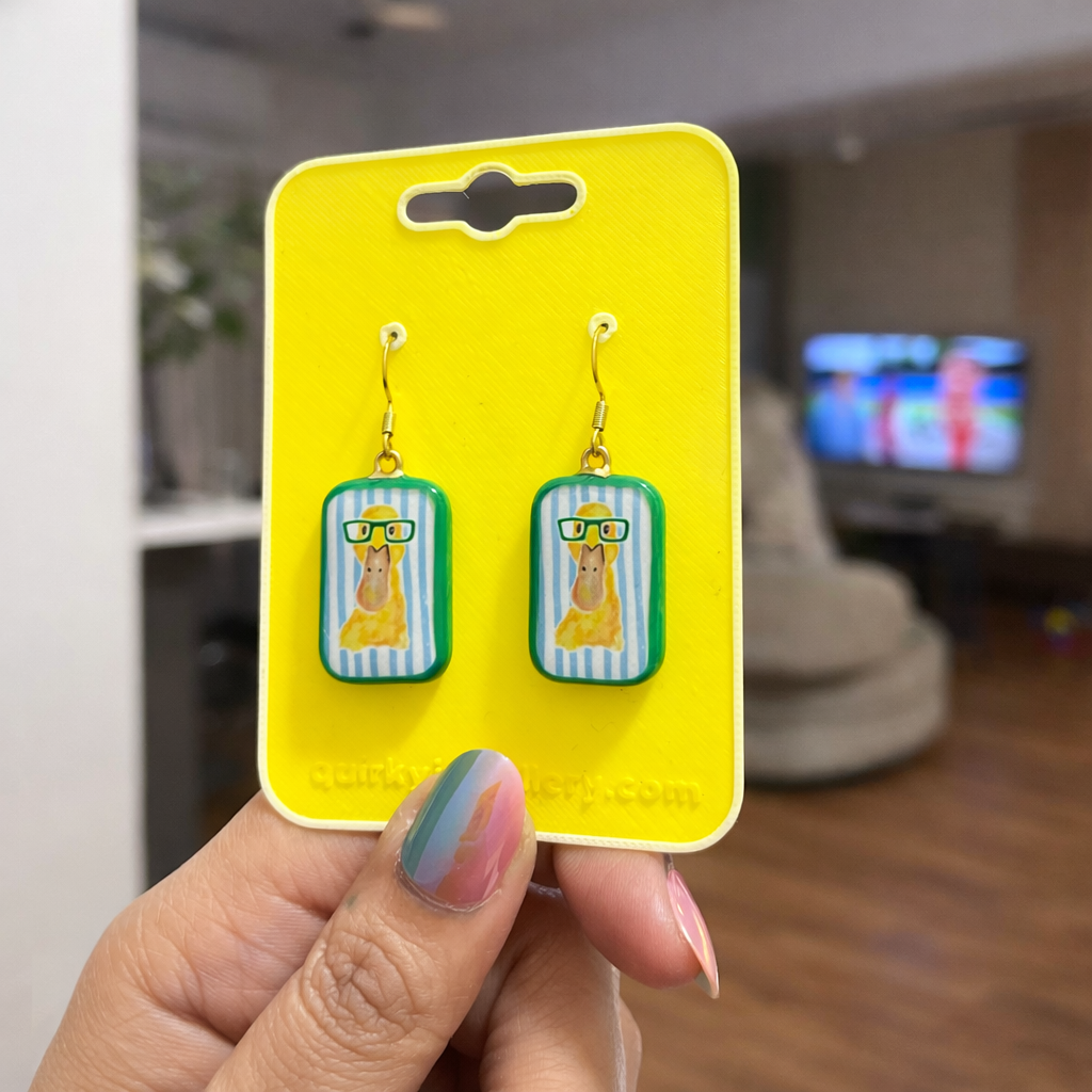 Earrings on a yellow card held by a hand in an indoor setting
