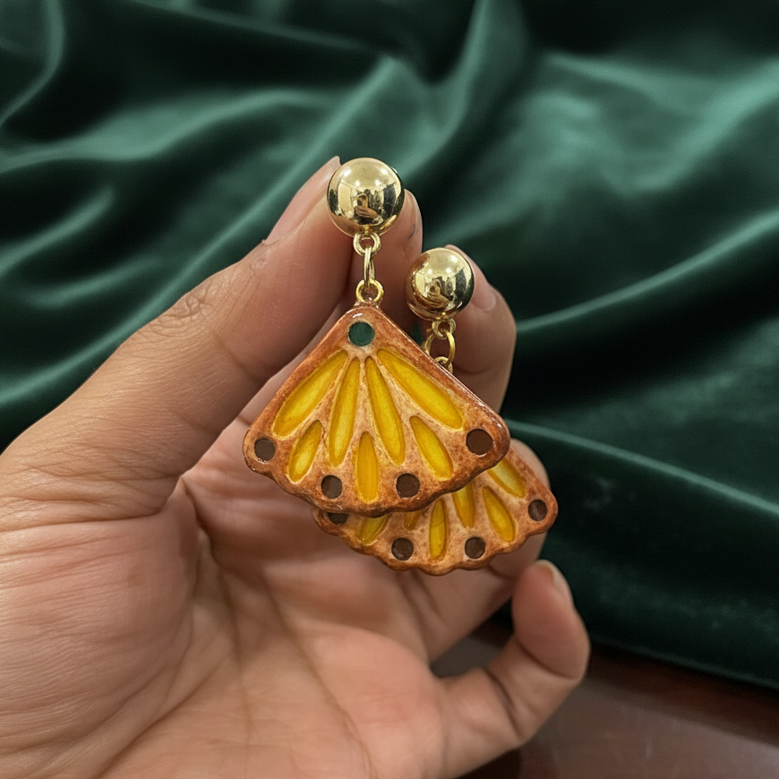Butterfly-shaped earrings with gold accents held against a green fabric background