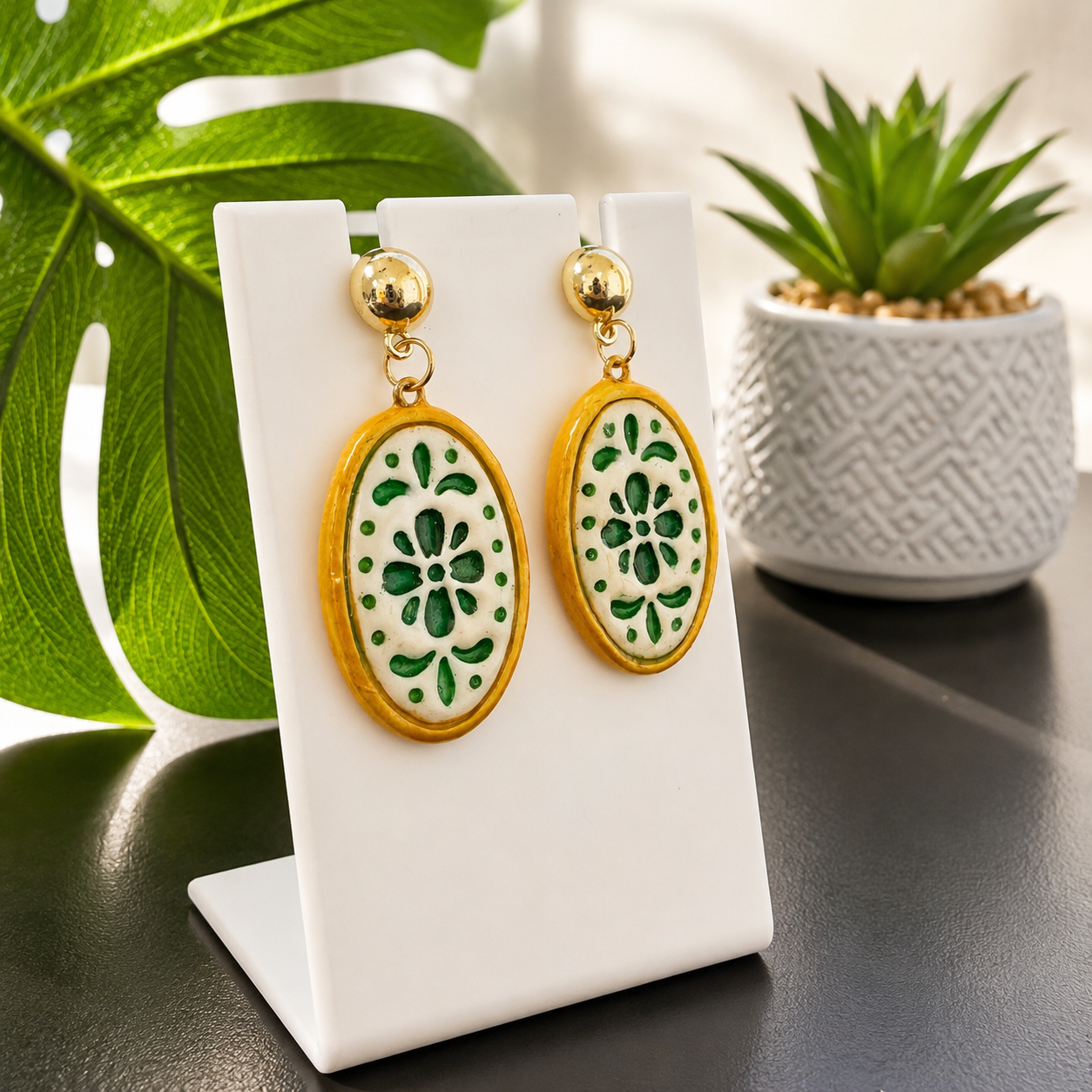 Pair of earrings with green floral design on a white stand with plants in the background
